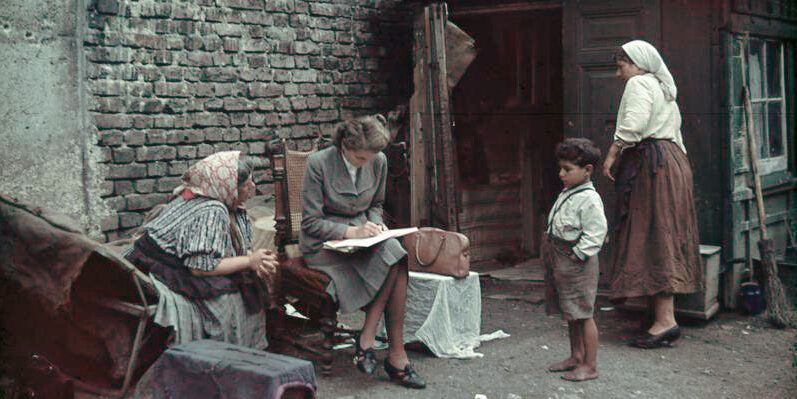 Eva Justin interviewing Romani women and children in Racial Hygiene Unit photograph taken between 1936 and 1940. [German Federal Archive – Digital image archive: R 165 Bild-244-72 https://commons.wikimedia.org/wiki/File:Bundesarchiv_R_165_Bild-244-72,_Eva_Justin_vor_Wohnung.jpg